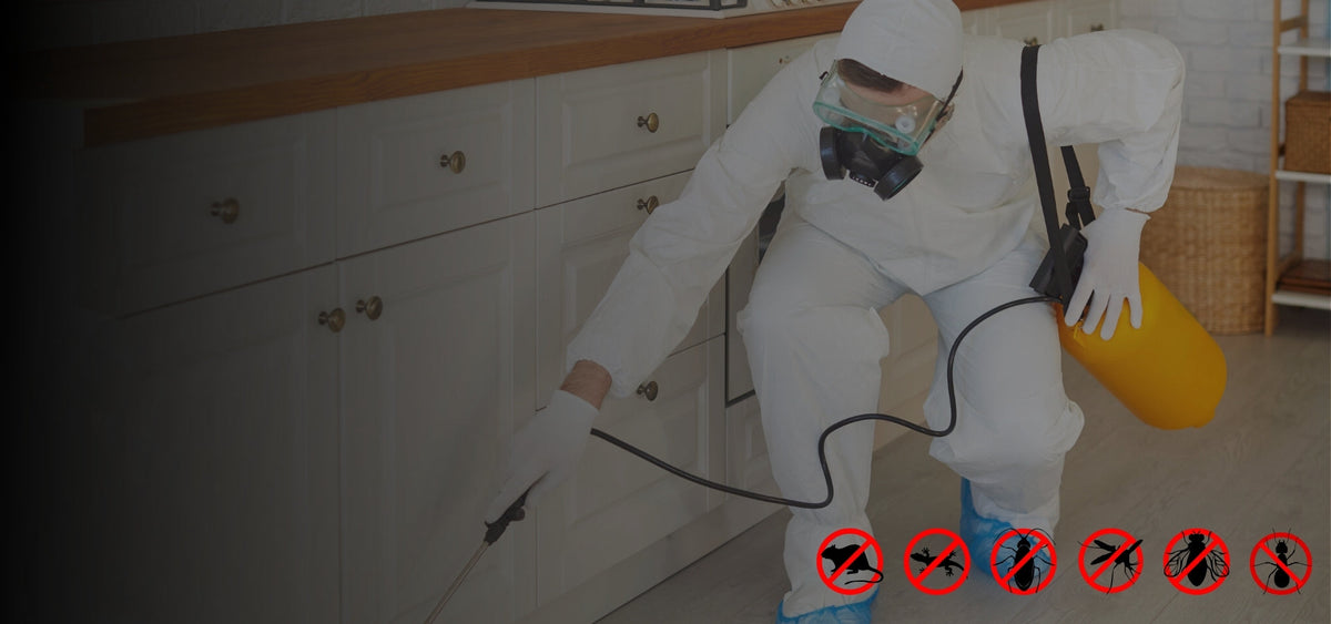 Pest control worker in a protective suit and mask spraying kitchen cabinets